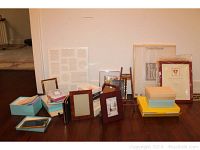 Photo showing multiple picture frames in wood tones and boxed stationery sets arranged on floor near wall.