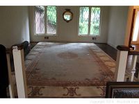 Large wool pile area rug laid out on hardwood floor, showing full size and shape with decorative borders and central medallion design in beige and brown color.