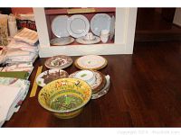 Overview of cups, saucers, dinner plates, and decorative bowls on hardwood floor with folded linens in background