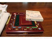 Photo showing large framed Monopoly board on table with Mid Life Crisis board game box on top.