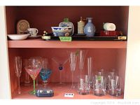 Wide shot of shelf showing entire lot including tray, salt and pepper, Asian vase, Wedgwood, clock, stemware, and rocks glasses