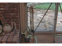 View of the fireplace tools set arranged by a window and adjacent to fireplace. Includes brass or bronze tools with duck-shaped handles and a fireplace screen leaning in the background.