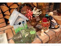 Photo showing assortment of items including birdhouse, small figurines, glass chunk, candle holder, large brass vase and clock arranged on red brick hearth