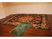Full view of the large floral area tapestry on floor with one green bath mat on top, showing size and edge condition.
