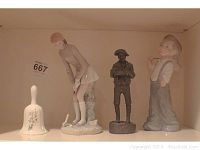 Shelf showing all four items: Lladro woman golfer, Michael Garman man statue, Zaphin boy figurine, and Stafford ceramic bell.