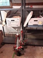 Two tall decorative topiaries about 40 inches tall. They have black square bases and are decorated with silver and red ornaments. One topiary shows visible damage to the top.
