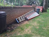 View of two fiberglass step ladders leaning against a brick wall outdoors, one with black and blue end caps