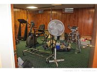 View of two rolling clothing racks in a basement room along with exercise equipment and a tall floor fan in center.