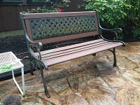 Front angle view of metal and wood outdoor yard bench on stone patio, showing lattice metal backrest and brown wood seat slats.