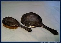 Full view of sterling silver brush and hand mirror with ornate floral detailing and natural bristles on brush.