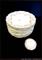 Stack of 12 white side plates with pink rose pattern around rim and center, plus round mustard pot with lid showing, set against a dark background.