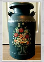 Front view of milk can showing hand painted floral bouquet with red, yellow, white flowers and green leaves with a silver decorative border near the top rim and metal handles.