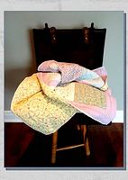 Quilt draped over chair showing folded fabric and patchwork details in pastel colors