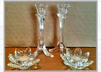 Two pairs of crystal candleholders including lotus votive and floral taper designs on cardboard background