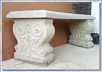 Front view of concrete garden bench showing detailed raised scroll motifs on legs and heavy base.