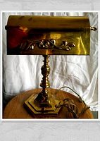 Full frontal photo of brass bankers lamp placed on wooden surface showing adjustable decorative shade and hexagonal base.