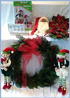 Image showing two floral wreaths with red poinsettia flowers, one larger faux cedar wreath with red bow, two bendable Christmas elves standing, and a handmade Old World Santa figure seated in the background.