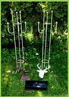 Two tall white metal candleholders each holding six candles with an iron deer head sculpture, armillary sphere, and black metal mailbox on grass with green foliage background.