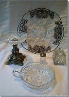 Photo showing assortment of serving pieces including crystal condiment pot with lid, salt shaker, serving plate, pedestal dish, and small condiment dish arranged on surface.