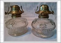 Pair of small clear pressed glass antique oil lamps with decorative embossing and brass burner fittings shown side-by-side.