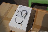 Artificial shark tooth necklace displayed on a white box, showing the black cord and white tooth pendant in plastic packaging.