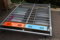 Metal bed frame shown with orange and light blue drawer fronts installed on one side, all drawers visible in different colors.