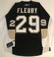 Rear view of black Pittsburgh Penguins jersey with white sleeves, gold trim, number 29 and nameplate ‘FLEURY’, autograph visible on back number, Reebok tag at hem.