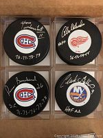 All four signed hockey pucks arranged in a 2x2 grid on a brown surface showing team logos and signatures visible.