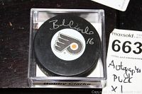 Top view of the autographed Philadelphia Flyers hockey puck inside a clear display case labeled 'Bobby Clarke'. The puck shows Bobby Clarke's signature.