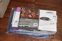 Packaged Salton portable cooktop, Montes World 57" grill cover, and folded blue tarp visible in clear plastic wrapping