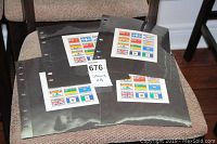 Four black protective album pages with sheets of Canadian flag stamps placed on a chair.
