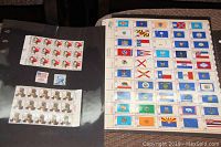 Two sheets of US postage stamps laid open on a flat surface. One sheet shows colorful state flags from the Bicentennial 1976 series. The second sheet includes other US-themed stamps.