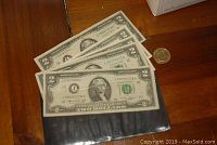 Six US $2 bills fanned out on a table with a US $1 coin placed separately.
