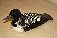 Front view of the hand-painted wooden loon sculpture showing black and white feather pattern, red eyes, and glossy finish.