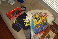 Photo of the two Smokin Joes Racing t-shirts and the two die cast model cars on a couch.