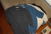 Five Tommy Bahama men's silk shirts hanging on hangers, laid out on a couch, showing colors and styles.