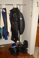 Full view of black leather snowmobiling jacket and pants on rack with snow boots and helmet on floor beneath them.