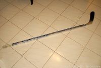Full length photo of the Easton Synergy hockey stick on floor showing taped handle and blade with stick shaft graphics.