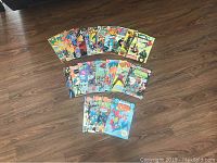 24 vintage DC comic books laid out on wooden floor showing different cover artwork.