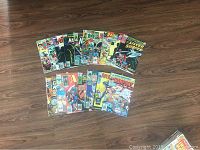 Photo showing approximately 20 old Marvel comic books laid out on a wooden floor. Titles include Avengers, Silver Surfer, and Champions with colorful vintage covers from the 1960s onward.