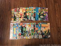 Two rows of older DC comic books on a wooden floor. Shows various titles including Green Lantern, Aquaman, The Unknown Soldier, Batman, Martian Manhunter, and Superman. Comics vary in cover condition with some bagged for protection.