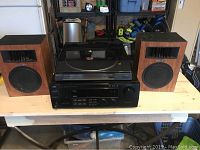 Wide view of the stereo setup showing the two wooden speakers, JVC receiver, and Hitachi record player on a wooden table.