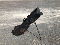 Black golf bag with stand legs on paved surface, showing the full bag profile