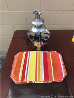 Full view of the fondue set and one of the orange and brown striped place mats on a table.