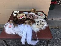Photo of assorted masks spread out on a folding table outside on gravel and concrete ground with a beige wall background