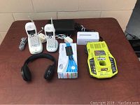 Photo showing two white cordless phones with chargers, black headphones, boxed black USB switch, white hard drive dock, and yellow Ryobi charger
