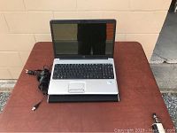 Front of open HP laptop on cooling pad showing silver keyboard area and touchpad, power adapter beside it.