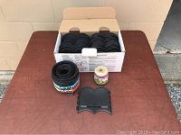 Box containing multiple black plastic garden edging pieces, alongside a roll of black plastic garden edging and a spool of beige twine on a table.