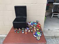 Wide shot showing black cube-shaped faux leather ottoman, dozens of colorful Skylander figurines arranged on table
