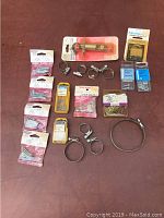 Photo showing assortment of hardware with hose clamps, latch bolt, cabinet locks, nails, and small fasteners mostly in original packaging.